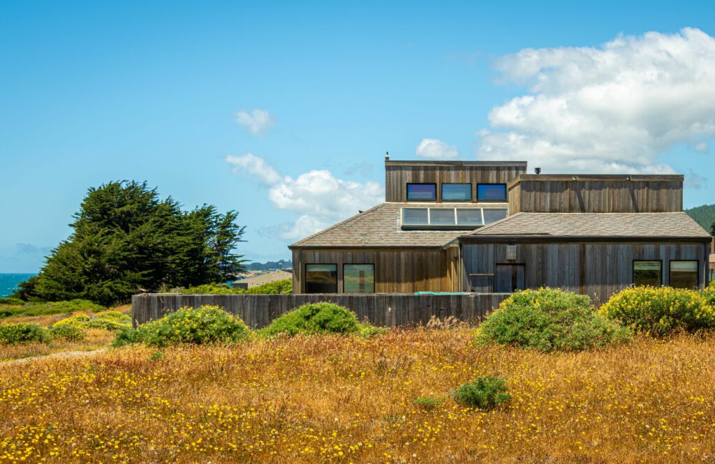 Cove Overlook: side outdoor view of home on meadow with blue sky and low bushes.