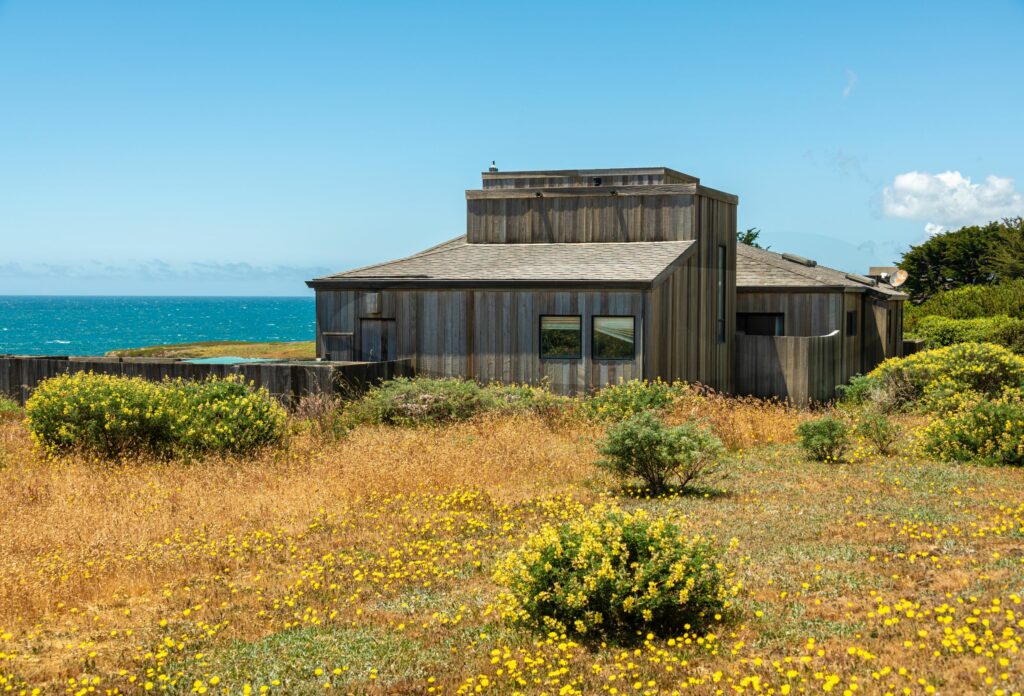 Cove Overlook: outdoor view of home on meadow with blue sky and view of ocean cove