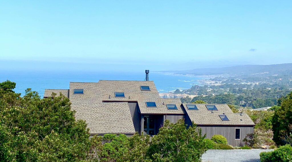 Starscape - exterior view of home surrounded by trees with view of ocean coast against blue sky.